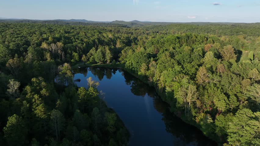 Idyllic tranquil lake surrounded by green forest trees at sunset. Beautiful calm nature landscape of USA in Virginia. Blue ridge mountains in distance. Suburb district of town.