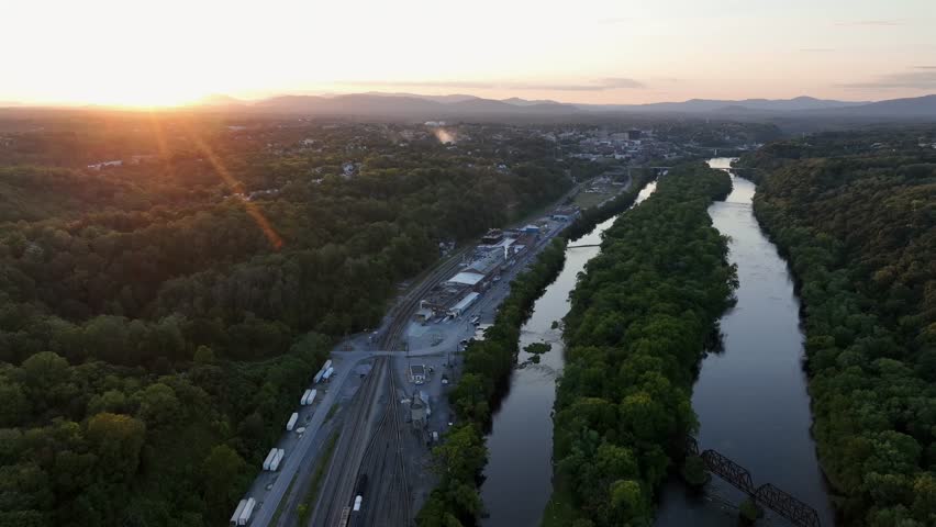 Railway tracks with parking cargo train near James River and sewage treatment plant in Virginia. Sun rays of golden sunrise in the morning. Aerial wide shot.