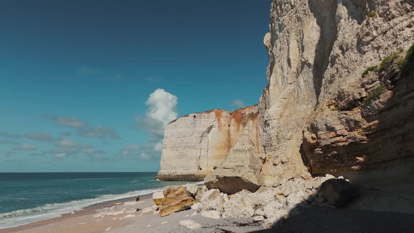 Ground-level view of massive chalk cliffs at Étretat with boulders on the beach, Normandy, France.