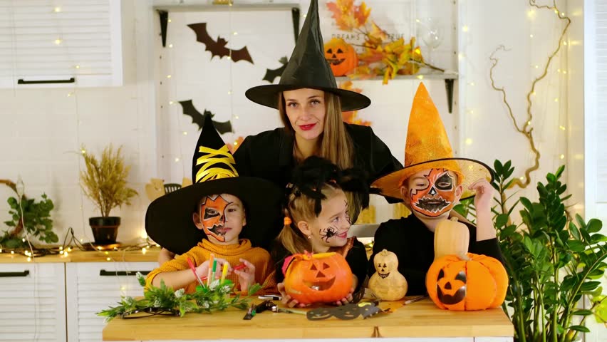 Halloween, a happy family a mother with children in festive costumes and makeup is preparing for Halloween at home in the kitchen by coloring and carving pumpkins and scaring everyone