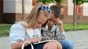 back to school. A girl and a boy play on a tablet in front of school and do homework and homework, first-graders brother and sister with briefcases or backpacks at school. The first day of school - Powered by Shutterstock - Get 15% off with code: PIKWIZARD15