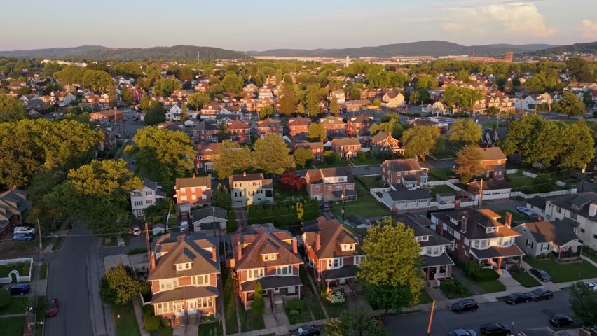 Residential neighborhood at golden hour, houses with green lawns and trees, with hills in background, Bethlehem, Pennsylvania, USA. Aerial forward