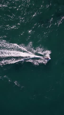 Top-down aerial view of a jet ski speeding across the deep blue sea, leaving a sharp white trail of foam. Dynamic drone footage of personal watercraft in motion