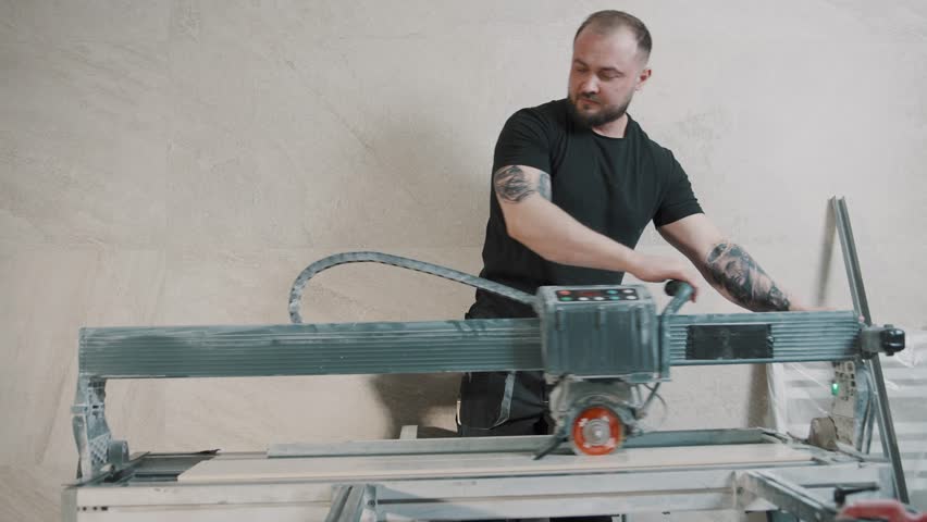 Man using tile cutter to prepare materials for floor installation in workshop