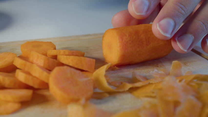 Close-up of mans hands chopping carrots on wooden cutting board.
