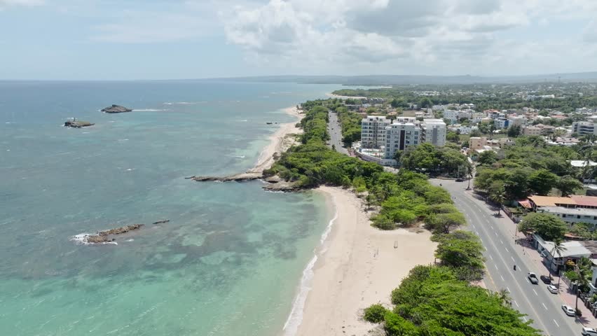 Puerto Plata coastline, sandy beach, coastal road, and city buildings, Dominican Republic. Aerial forward