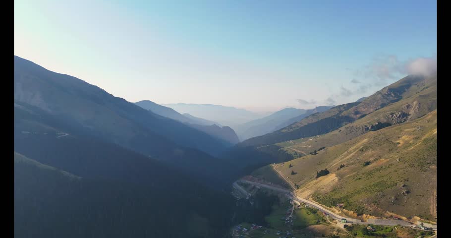 4K aerial drone view of mountain valleys in Trabzon highlands, Turkey. Scenic panoramic landscape with winding roads, hills, and peaceful natural beauty under clear blue sky.
