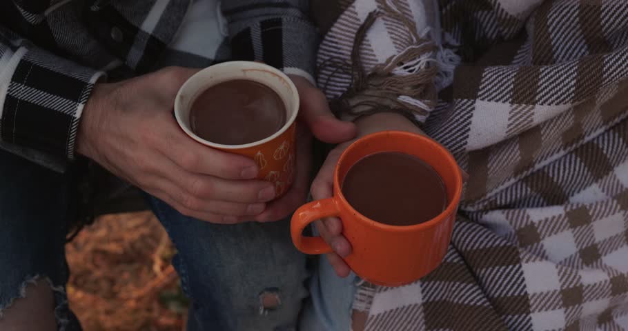 Young couple hands holding coffee cups under a plaid at the cozy autumn day