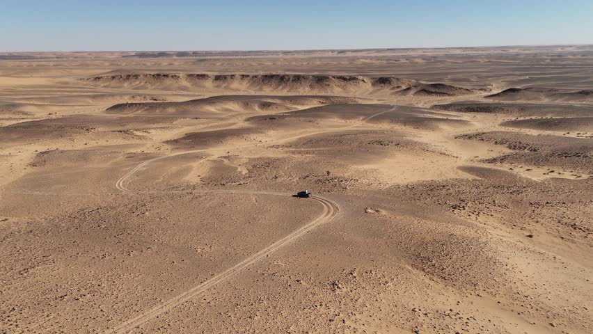 jeep car 4x4 driving around the Eye of the Sahara, also known as the Richat Structure in Mauritania, Sahara desert landscape aerial drone footage