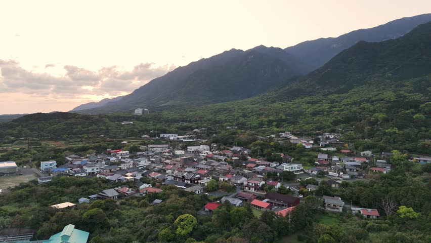 Aerial view of Onoaida in Yakushima, Japan, featuring clustered village houses, lush green forest surroundings, and dramatic mountains in the background under a calm evening sky with soft sunset light