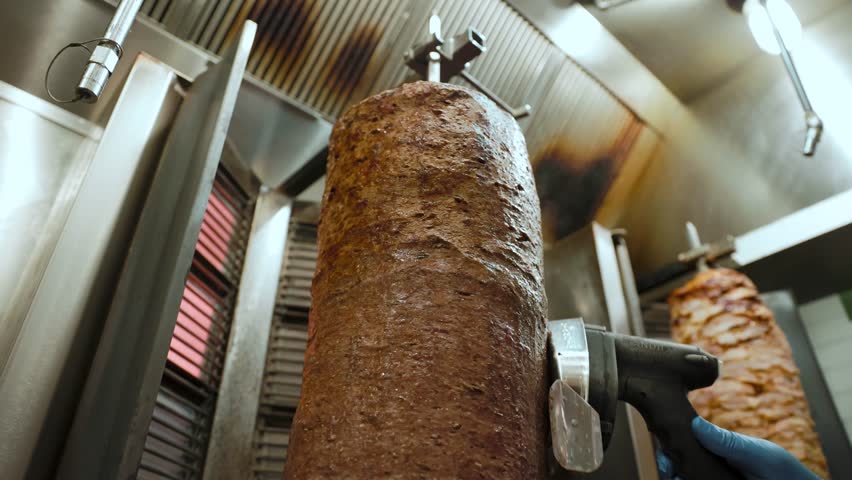 Chef slices meat from a rotating doner kebab indoors. Ideal for restaurant, culinary preparation, and Middle Eastern cuisine themes, highlighting food craftsmanship and meal presentation.