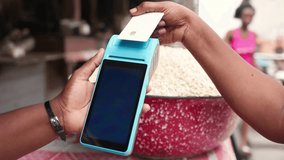 Contactless payment success, customer makes a transaction with a credit card via blue point of sale, POS terminal in a bustling outdoor African local traditional grains market. - Powered by Shutterstock - Get 15% off with code: PIKWIZARD15