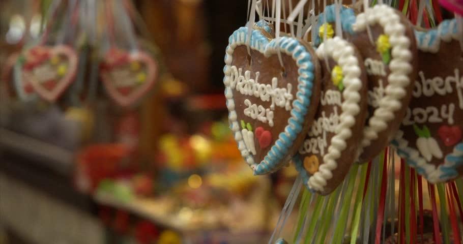 Oktoberfest cookie heart with blurred background shows traditional German celebration. Oktoberfest cookie detail includes white icing and hanging decoration, moving camera
