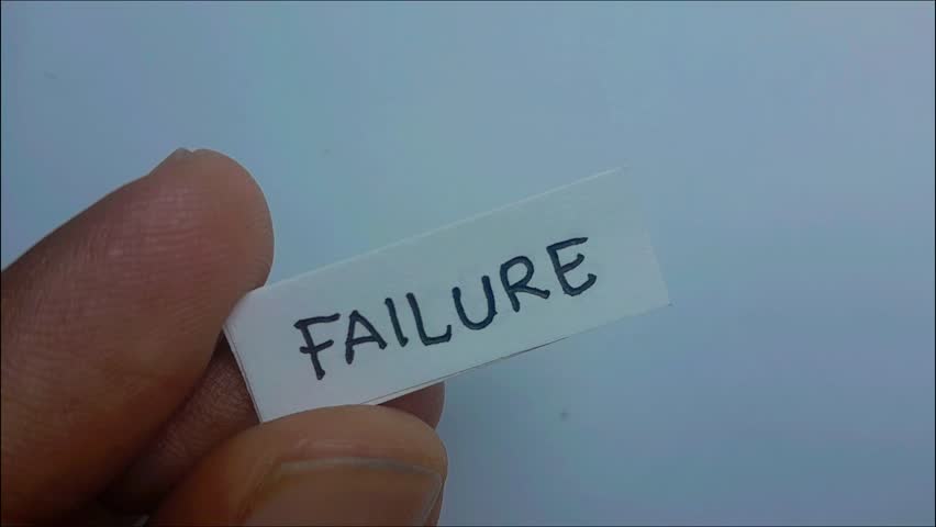 A pair of hands holds a paper with the word "FAILURE." As the paper is lifted, another paper beneath it reveals the word "SUCCESS." The hands place the "SUCCESS" sign in the center of the frame.