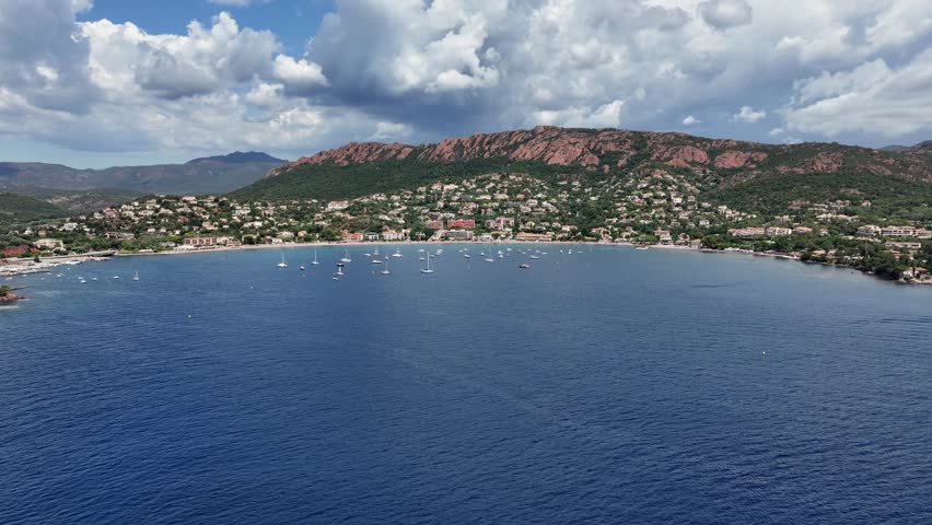flying across Agay Bay, French Riviera (Côte d'Azur) with Beach  "Agay Plage" cityscape of Saint-Raphaël and bright red mountains from "Massif de l'Esterel" in background - 4k aerial video footage