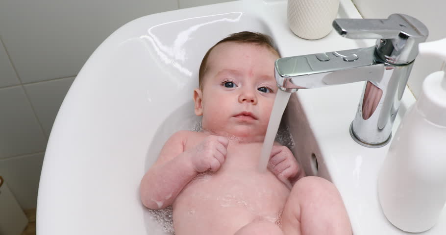 A caring father washes his baby girl in the sink