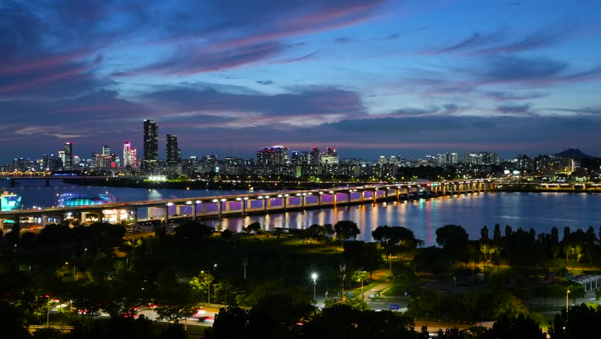 A beautiful summer sunset time lapse of the bustling Seoul skyline, showing vibrant city traffic on Banpo Bridge, the famous Rainbow Fountain, and the lights of Hangang Park along the Han River