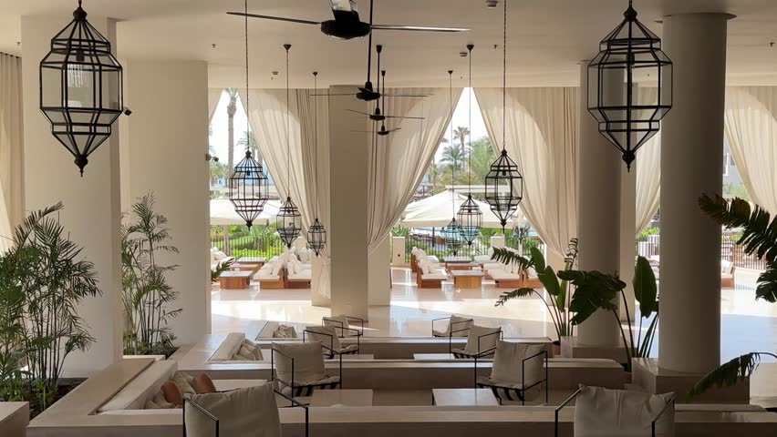 Egypt Hurhada August 07 2025.A sophisticated luxury hotel lobby with minimalist design, large arched windows, elegant white seating areas, lush plants, and traditional Middle Eastern-style lanterns.