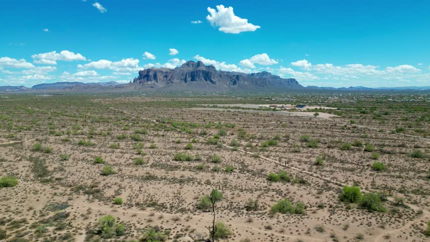 A drone shot of Superstition Mountains towering over the wide Arizona desert under a bright blue sky, USA