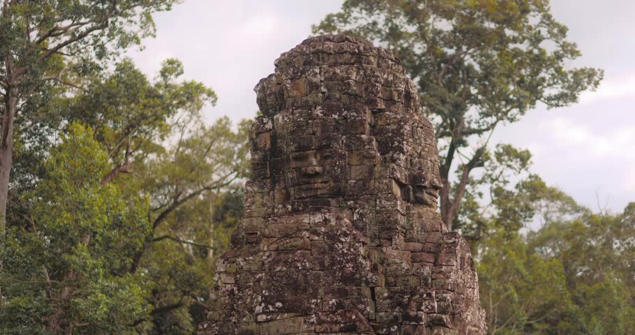 Majestic cinematic footage of Bayon Temple face tower rising above the tropical jungle in Angkor, Cambodia. Ideal for cultural promo, travel advertisements, history documentaries and tourism projects.