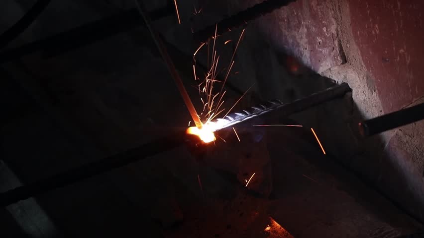 Welding work using electrodes. Welding two bars of reinforcement to create a frame for stairs in the country. Repair and construction work close-up. A person welds metal parts. Flash from welding work