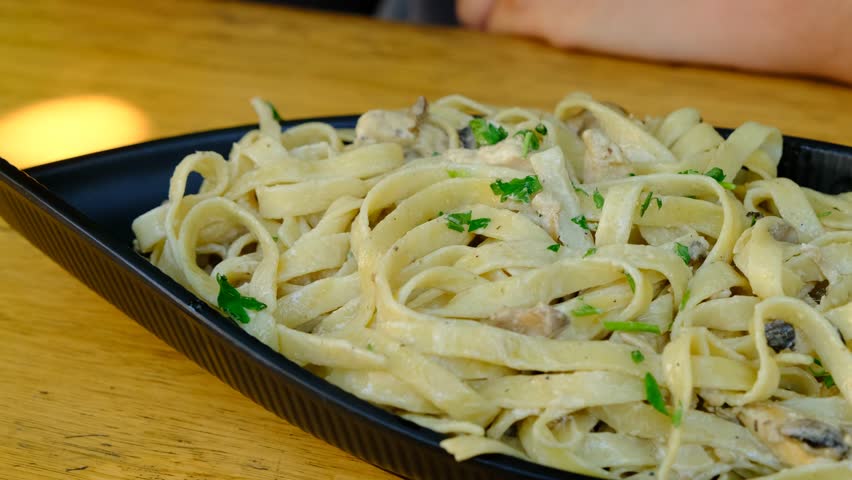 Close-up of Fork Twisting Fettuccine Alfredo with Chicken and Mushrooms. Delicious Creamy Pasta with Chicken and Mushrooms. Creamy Chicken Mushroom Fettuccine Pasta.