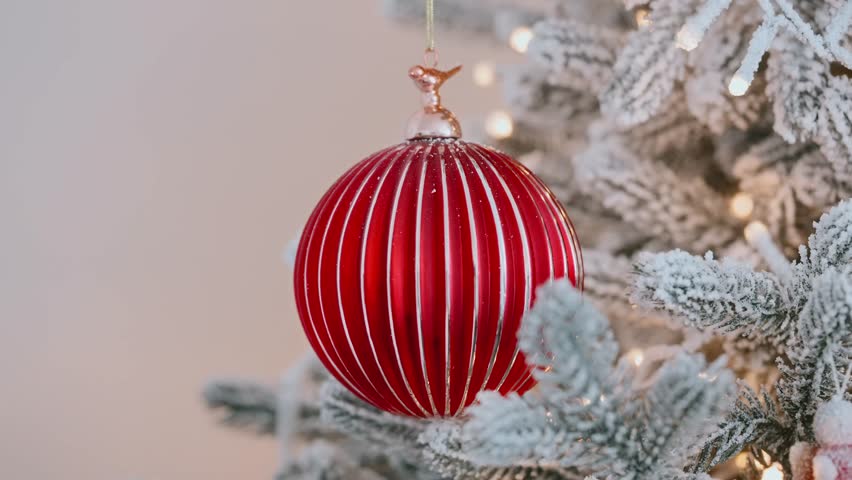 Christmas red ornament close-up hanging on beautifully lit Christmas tree flickering light. Festive bauble is surrounded by glowing string lights pine branches, creating warm cozy holiday atmosphere. - Powered by Shutterstock - Get 15% off with code: PIKWIZARD15