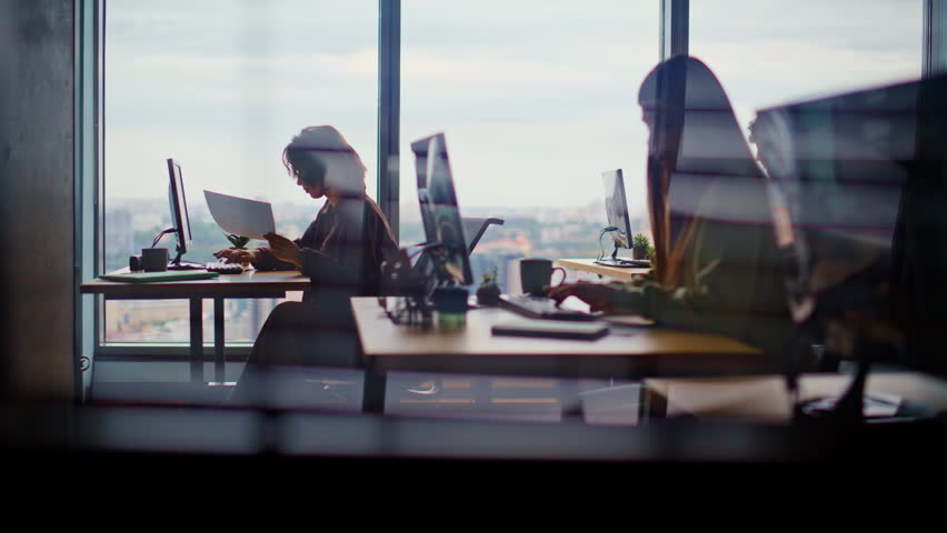 Busy corporate office silhouettes at cityscape window place closeup. Young people working computers feeling involved at creative agency. Men women writing emails typing keyboards together at coworking