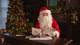Merry Christmas. Happy Santa Claus reading letters from children in festive Christmas living room. Santa with xmas wish list letter on Christmas eve. Mail of Santa Claus. Winter Holiday Celebrations - Powered by Shutterstock - Get 15% off with code: PIKWIZARD15