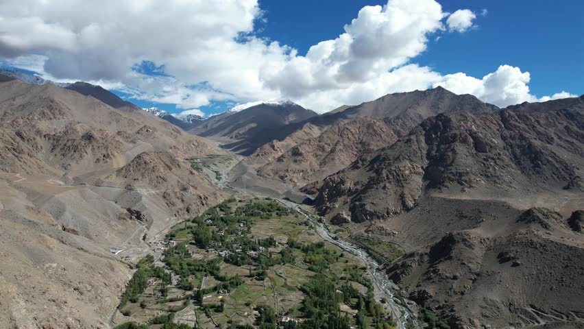 Aerial drone footage of Phyang village in Ladakh, India, showcasing traditional ice stupas formation area surrounded by dramatic Himalayan mountain landscape. Scenic view of barren mountains.