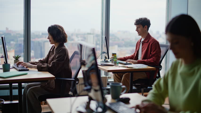 Young programmers coding computers sitting together at spacious coworking zone. Focused students learning software development practicing tasks. People typing keyboards actively at modern workspace