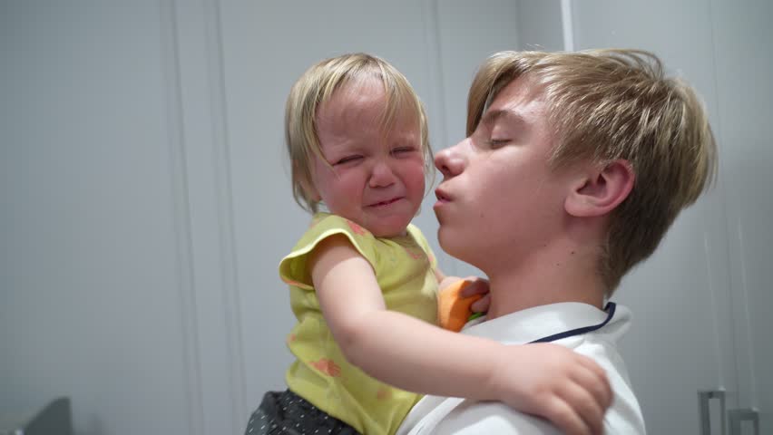 Young child gently comforts crying toddler sibling with tender, supportive embrace during emotional and heartfelt moment