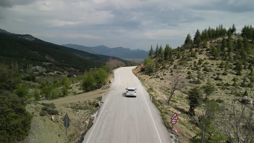 Drone view of a car on a curvy road in Turkiye. Dense forests and misty hills in Turkey. Scenic landscape full of vibrant greens and highland beauty. Ideal for nature and travel visuals.