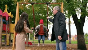 Parents, dad mom young daughter swing on swing in autumn park. Happy family, child outdoors, weekend. Child girl, sits on swing smiles. Father mother child girl play together on playground in autumn - Powered by Shutterstock - Get 15% off with code: PIKWIZARD15