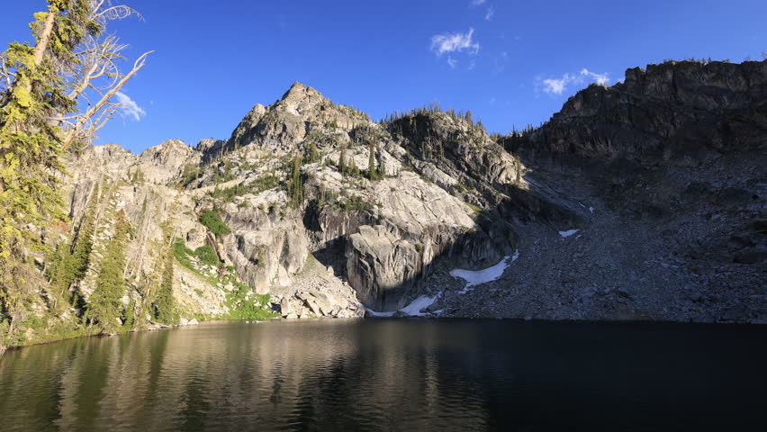 Lower Trail Creek Lake in Sawtooth National Forest in Idaho at dusk, where drifting summer clouds reflect off calm waters beneath rugged mountain peaks.