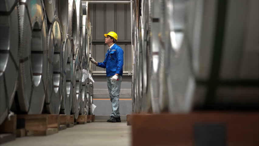 Industrial worker inspecting inside a large metal tube in a factory wearing safety helmet and gloves