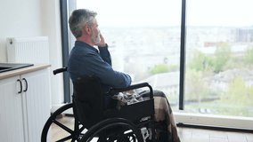 Senior Caucasian man sitting in wheelchair by kitchen indoors using phone near window. Scene depicts everyday lifestyle, accessibility, comfort, connection, communication, independence, and inclusion - Powered by Shutterstock - Get 15% off with code: PIKWIZARD15
