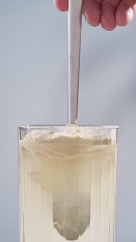 human hand mixing protein powder with water in glass.  whey sports nutrition. dry mixture for preparation of sporting or dietary drink.