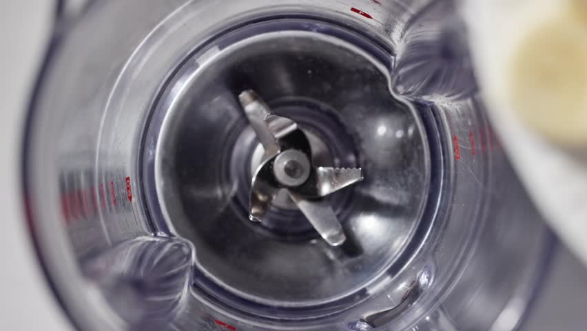 fresh raw sweet banana pieces falling in blender container  for making healthy breakfast smoothie, milkshake ingredients closeup, food slow motion in light kitchen