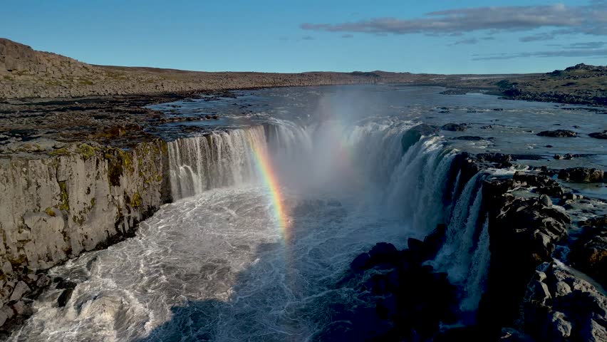 Witness the breathtaking cascade of Selfoss near Dettifoss, where the power of nature creates a stunning display. A vibrant rainbow arcs over the waterfall, enhancing the serene landscape of Iceland.