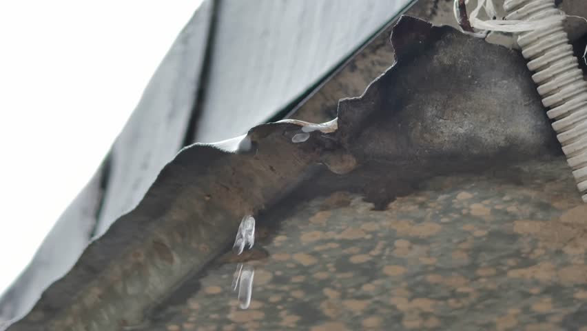 Macro close-up shot in slow motion of water droplets forming and falling from the edge of a corroded metal roof. Captures the detailed texture of the rusty surface and transparent liquid. - Powered by Shutterstock - Get 15% off with code: PIKWIZARD15
