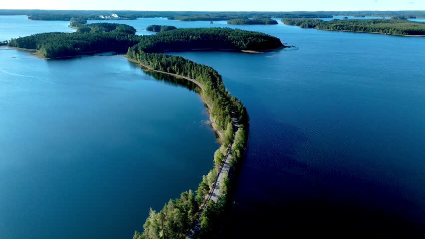 Marvel at the winding esker roads formation of Punkaharju, Finland, where lush greenery meets crystal-clear waters under a bright sky. Experience the serene beauty of this unique landscape.
