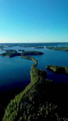 Experience the breathtaking beauty of Punkaharju in Finland, where a lush green esker road beautifully contrasts with the shimmering blue waters of Lake Puruvesi under a clear sky.