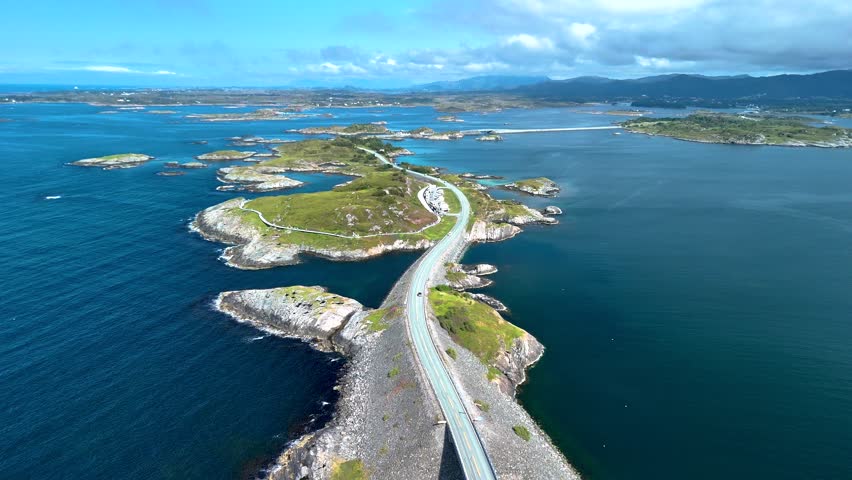 Witness the incredible Atlantic Ocean Road winding through breathtaking landscapes in Norway, showcasing the stunning coastal scenery with azure waters and dramatic skies during a sunny day.