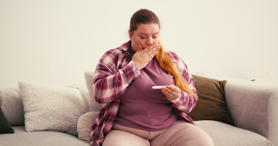Overweight Plus Size Woman holds pregnancy test anxiously examining result. Female shows extremely happy emotions after seeing positive picture in kitchen