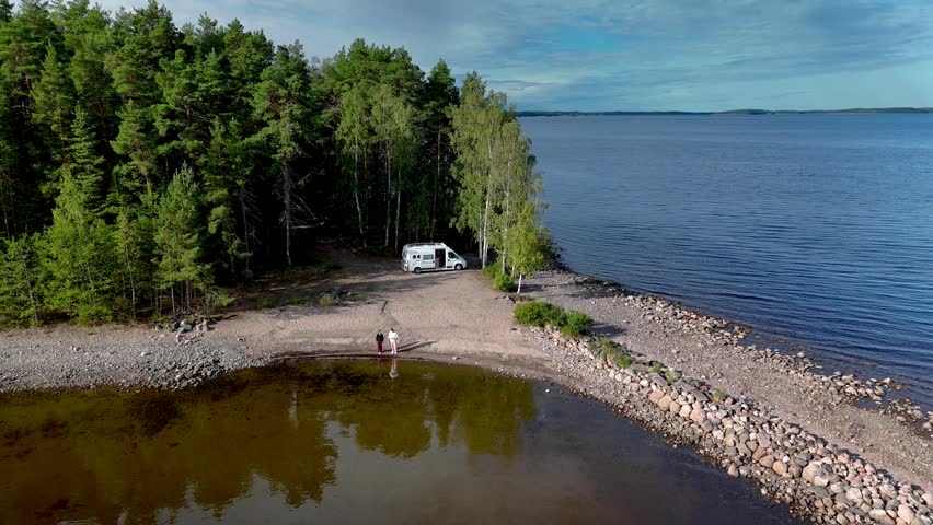 A peaceful campsite rests along shimmering water. Lush greenery envelops the area, creating an idyllic retreat for adventurers and families alike. a camper van parked by the Saimaa lake in Finland