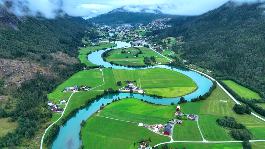 Nestled in the heart of Norway, Stryn showcases sprawling green fields, meandering rivers, and picturesque mountains under a cloudy sky. A serene haven for nature lovers and adventurers alike.