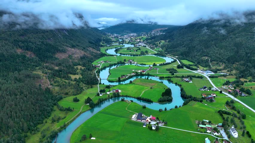 Explore the breathtaking beauty of Stryn, Norway, featuring winding rivers that traverse vibrant green fields under cloudy skies. A picturesque scene displaying natures tranquility.