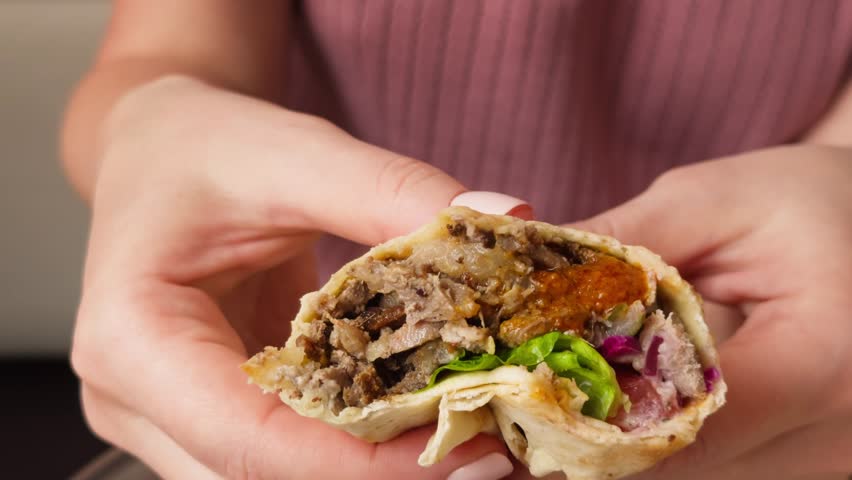 Spicy doner kebab or shawarma in hands, with fried meat, fresh salad and vegetables with sauce. High quality 4k footage