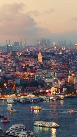 Vertical view of the historic Galata Tower standing out among the illuminated rooftops and modern skyscrapers of Istanbul's skyline at sunset